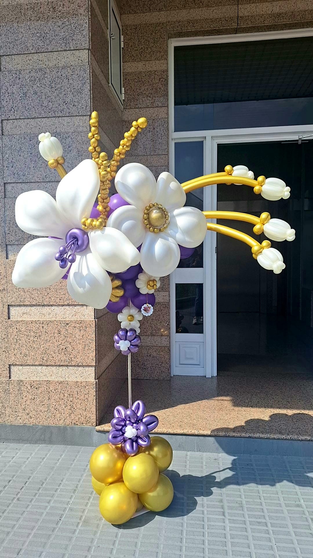 Arreglo floral de globos blanco, morado y dorado hecho por una alumna Glover