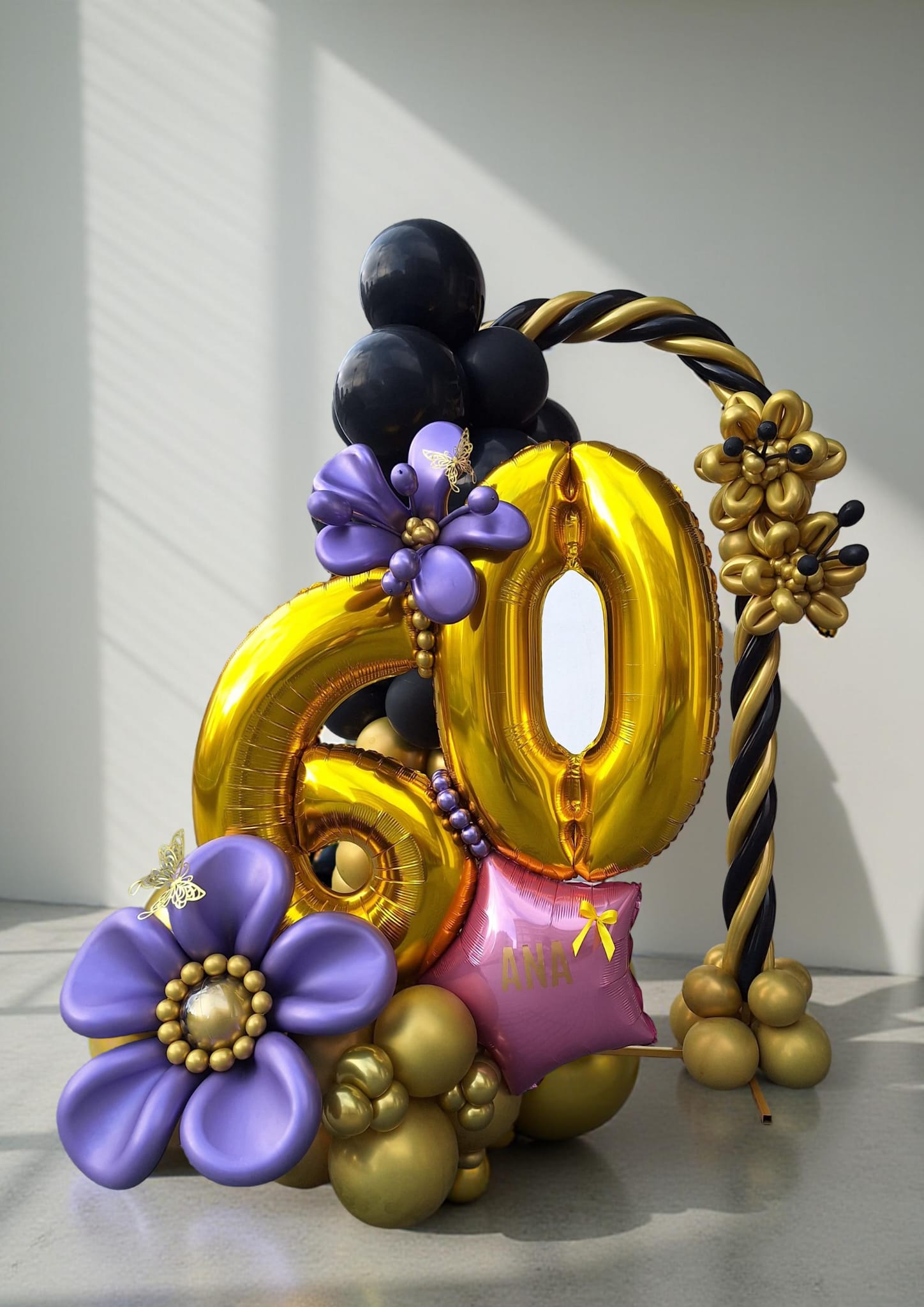 Decoración de globos dorada, negra y morada con número 60 hecha por una alumna Glover